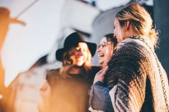 three female friends standing near each other laughing