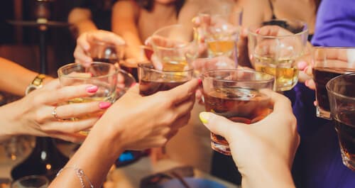 hands holding glasses filled with alcohol toasting in celebratory fashion