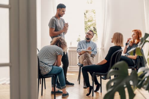man standing surrounded by peers at group therapy