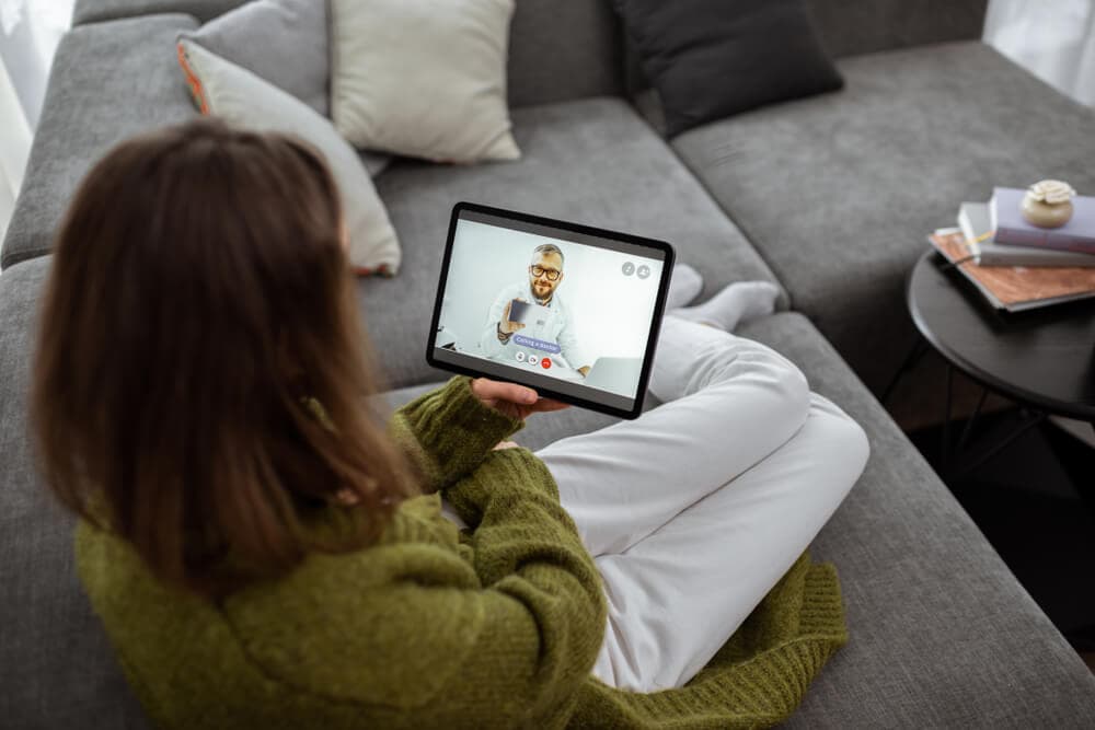 woman sitting on couch meeting with medical professional virtually