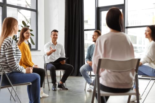 Small group of people sitting in chairs at group therapy for addiction treatment