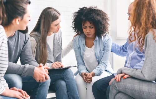 Group of young adults in therapy supporting a young woman who is upset