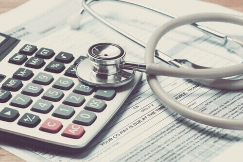 photo of a calculator and stethoscope sitting on top of medical bills
